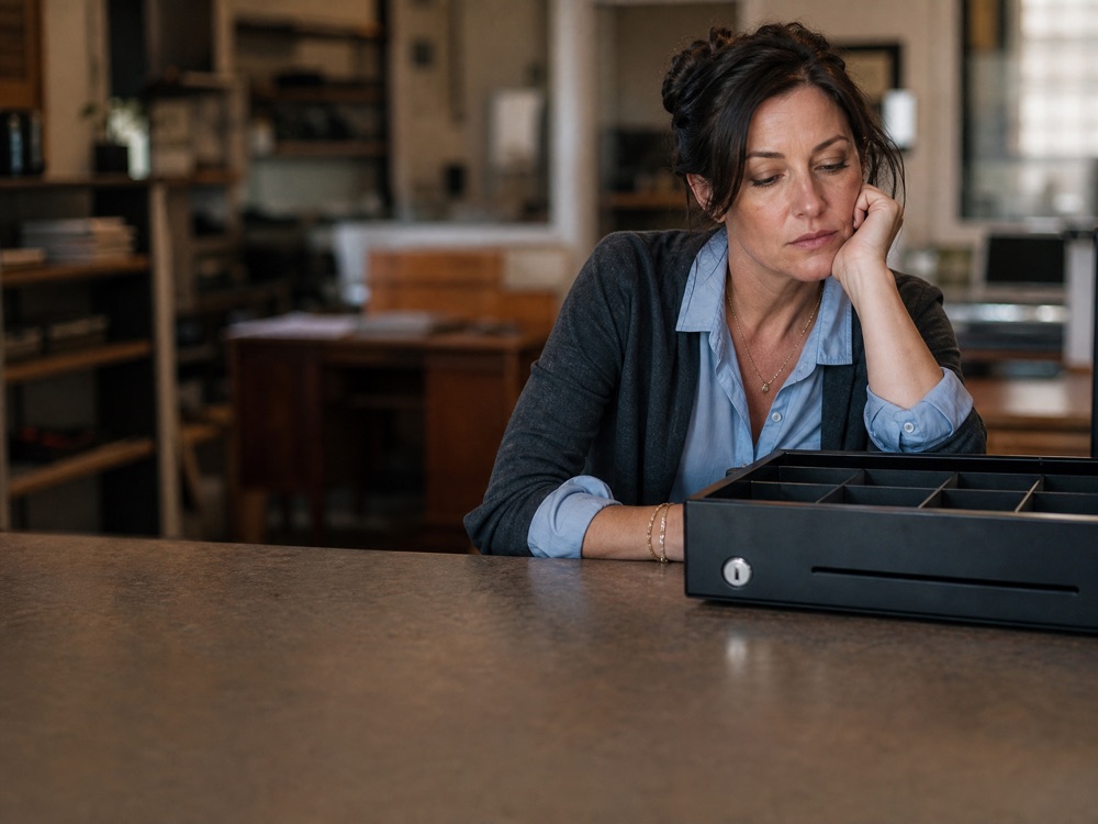 A business owner at a desk beside a nearly empty cash drawer