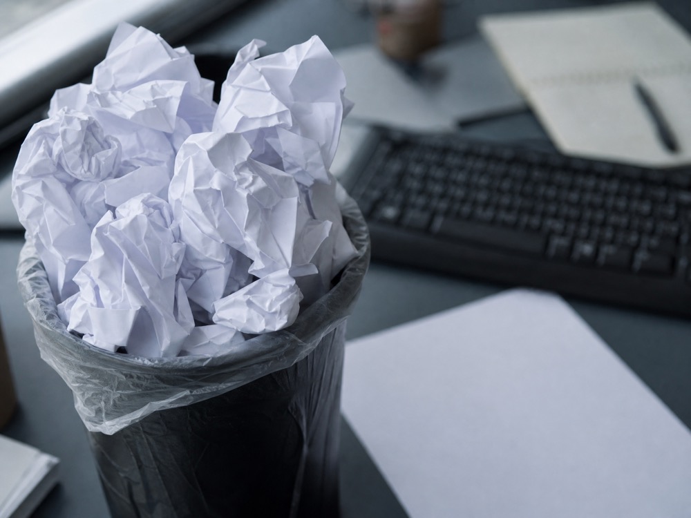 A trash bin overflowing with crumpled drafts beside a keyboard